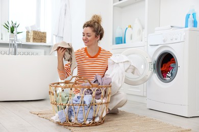 Photo of Happy woman with laundry near washing machine indoors