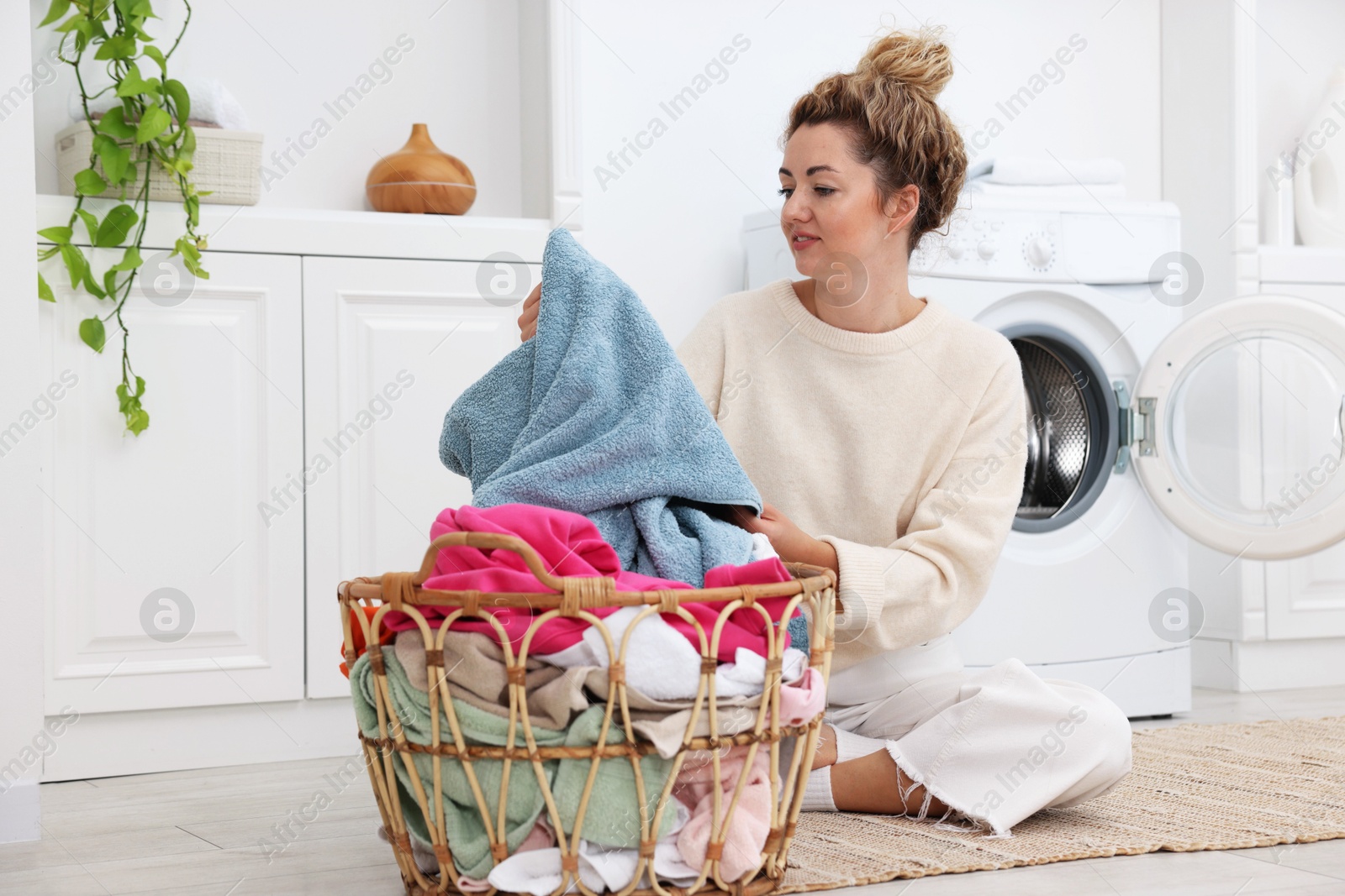 Woman with laundry near washing machine indoors Photo of Woman with laundry near washing machine indoors