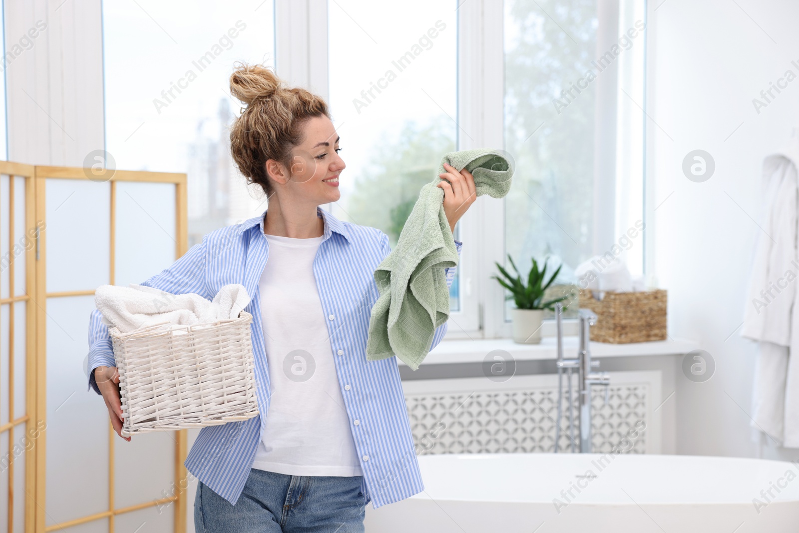 Photo of Woman with basket full of laundry indoors, space for text