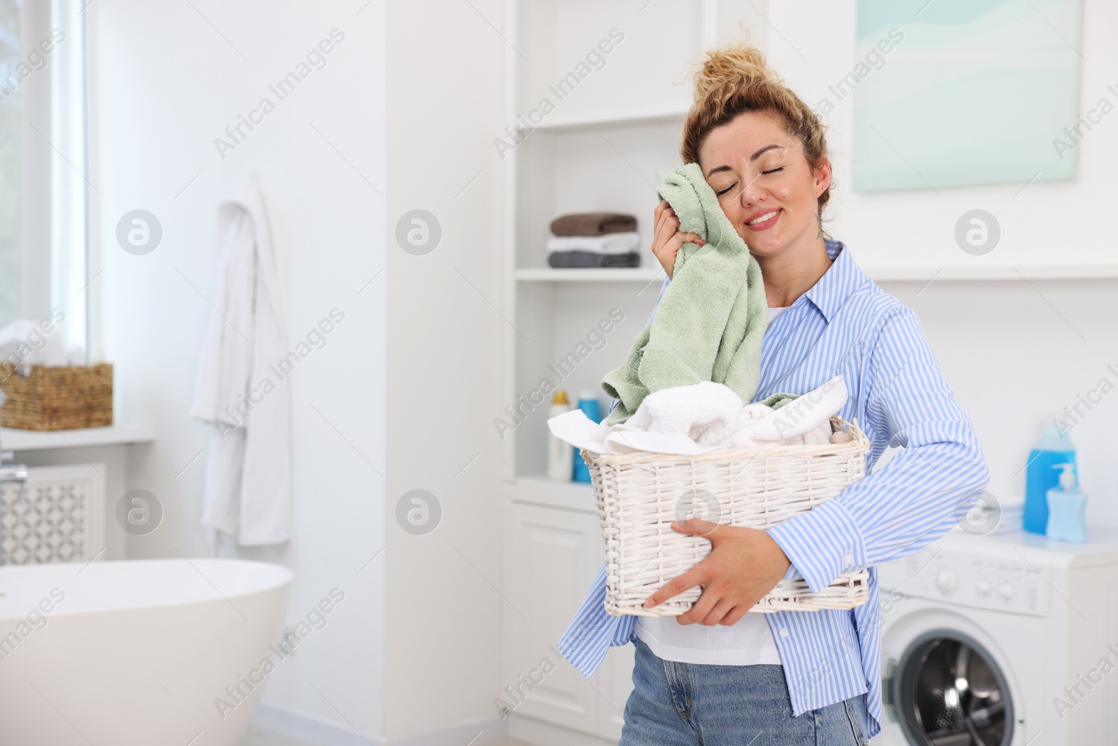 Photo of Woman with basket full of laundry indoors, space for text