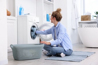 Photo of Woman putting dirty laundry into washing machine indoors