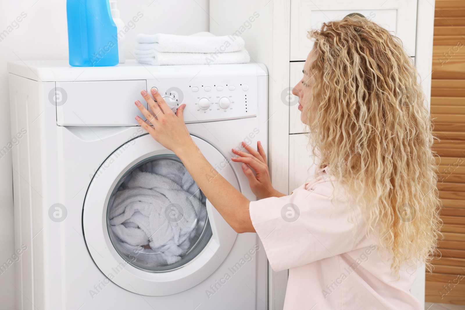Photo of Woman using washing machine indoors, closeup. Laundry day