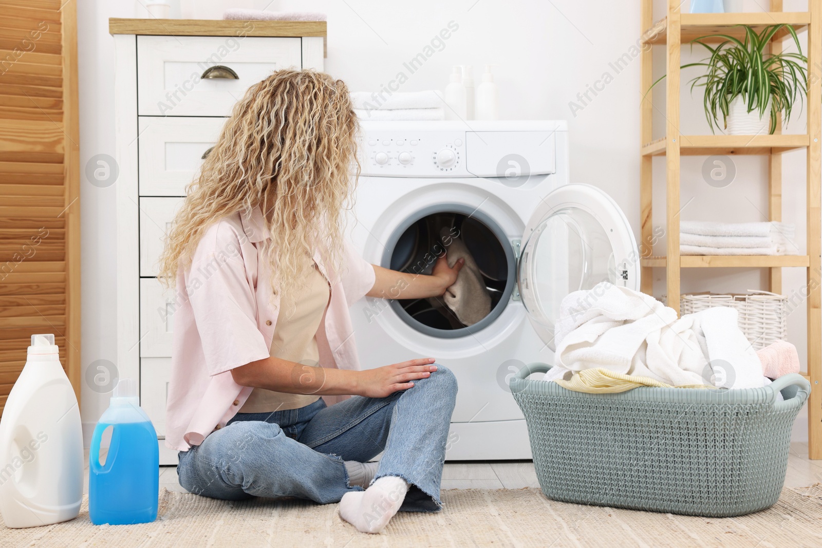 Photo of Woman putting dirty laundry into washing machine indoors