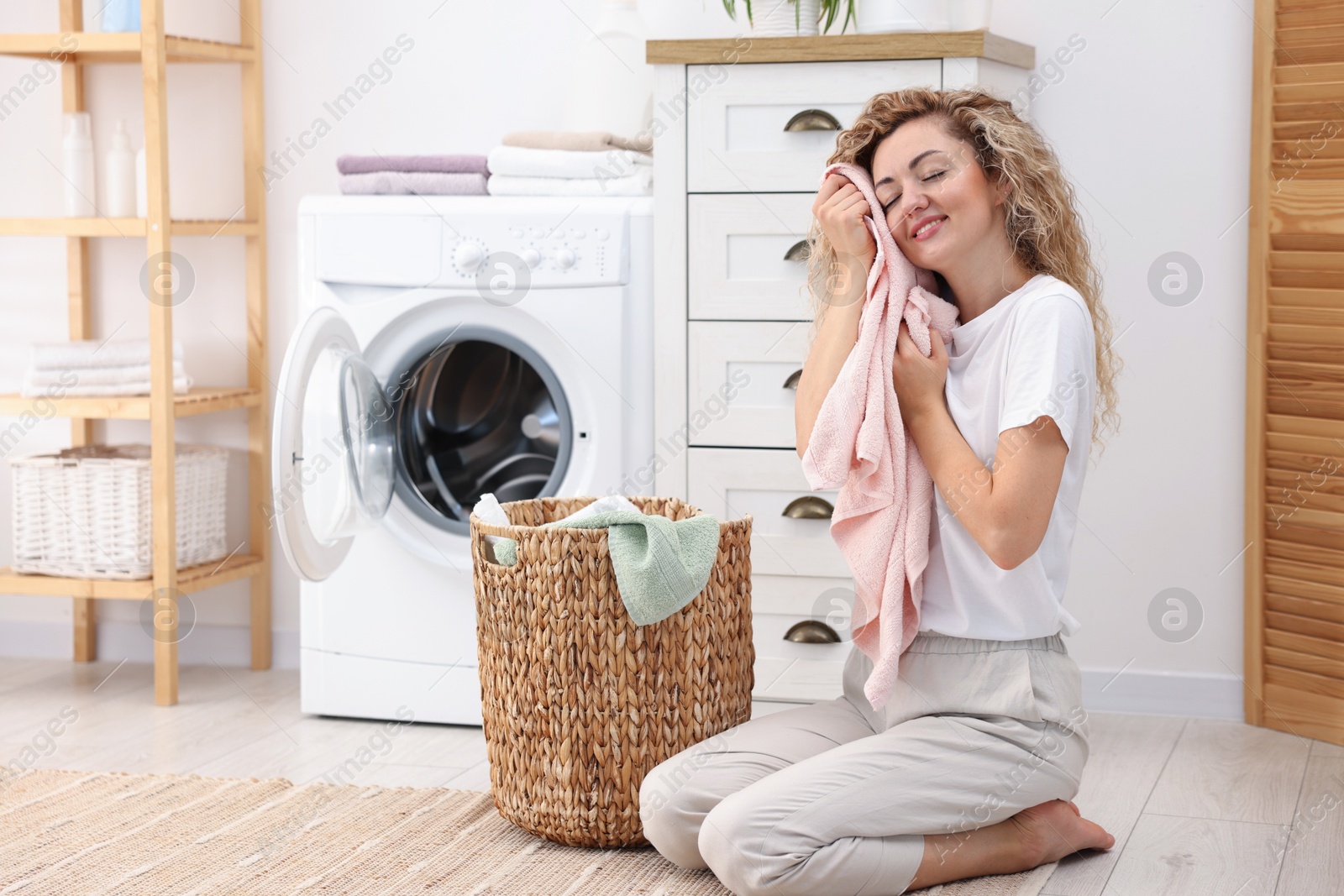 Woman with clean laundry near washing machine indoors Photo of Woman with clean laundry near washing machine indoors