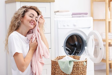 Photo of Woman with clean laundry near washing machine indoors