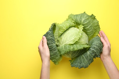 Photo of Woman with fresh Savoy cabbage on yellow background, top view. Space for text