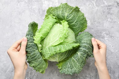 Photo of Woman with fresh Savoy cabbage at grey textured table, top view