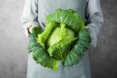 Photo of Woman holding fresh Savoy cabbage on grey background, closeup