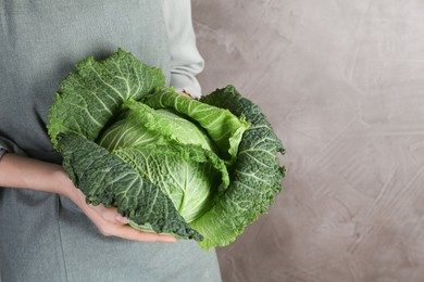 Photo of Woman holding fresh Savoy cabbage on grey background, closeup. Space for text