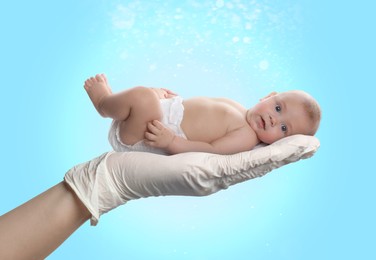 Image of In vitro fertilization (IVF). Cute little baby in doctor's hand against light blue background