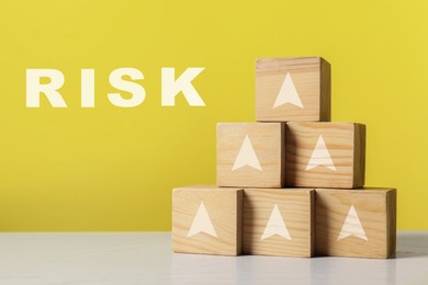 Image of Risk. Pyramid of wooden cubes with arrows against yellow background