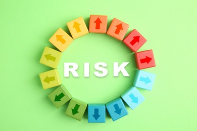 Image of Word Risk surrounded by colorful wooden cubes with arrows on light green background, top view
