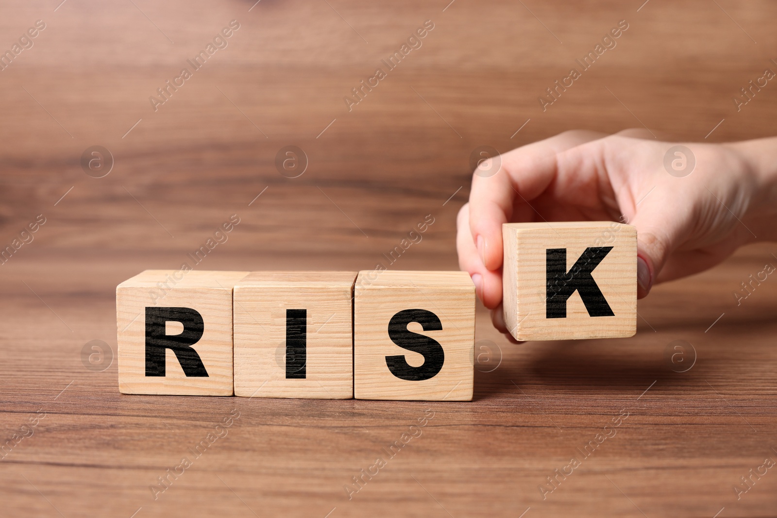Image of Woman putting wooden cube with letter K to make word Risk at table, closeup