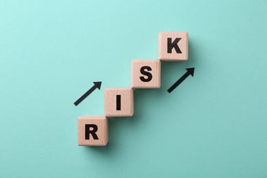 Image of Word Risk of wooden cubes with letters and arrows on turquoise background, top view