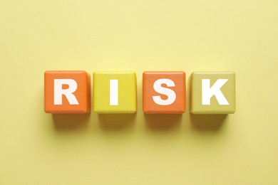 Image of Word Risk of wooden cubes with letters on pale yellow background, top view