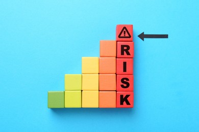 Image of Word Risk of wooden cubes with letters on light blue background, top view. Arrow pointing at warning sign