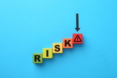 Image of Word Risk of wooden cubes with letters on light blue background, top view. Arrow pointing at warning sign