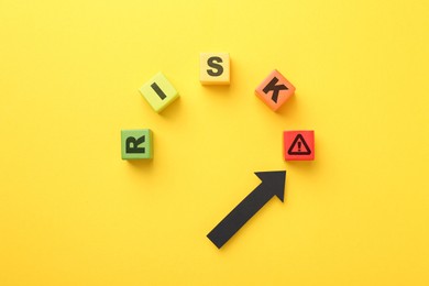 Image of Word Risk of wooden cubes with letters on orange background, top view. Arrow pointing at warning sign