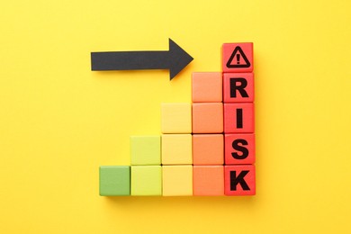 Image of Word Risk of wooden cubes with letters on orange background, top view. Arrow pointing at warning sign