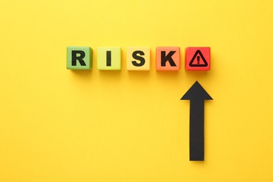 Image of Word Risk of wooden cubes with letters on orange background, top view. Arrow pointing at warning sign