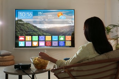Image of Woman watching TV using video projector at home in evening. Menu with icons and information on screen