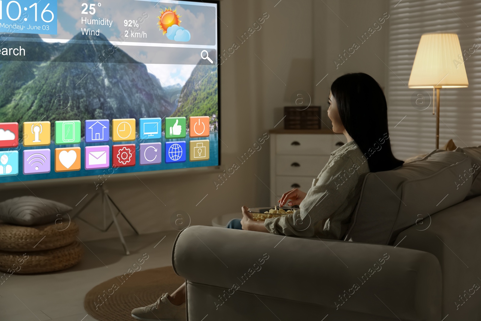 Image of Woman watching TV using video projector at home in evening. Menu with icons and information on screen