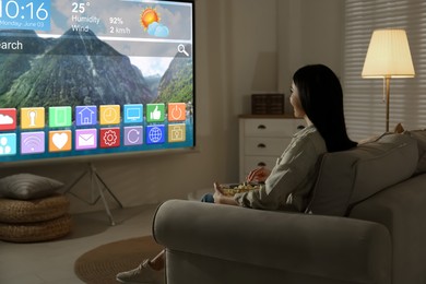 Image of Woman watching TV using video projector at home in evening. Menu with icons and information on screen