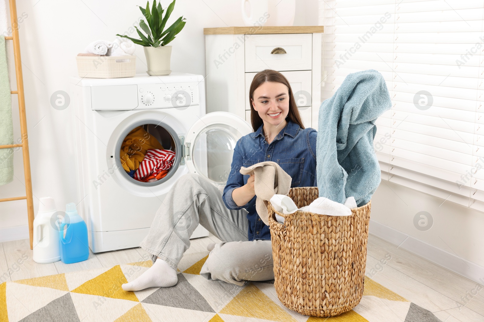 Woman with laundry near washing machine indoors Photo of Woman with laundry near washing machine indoors