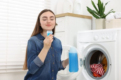 Photo of Woman with detergent near washing machine indoors. Laundry day