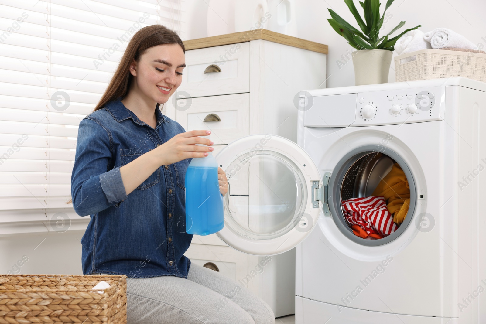 Photo of Woman with detergent near washing machine indoors. Laundry day