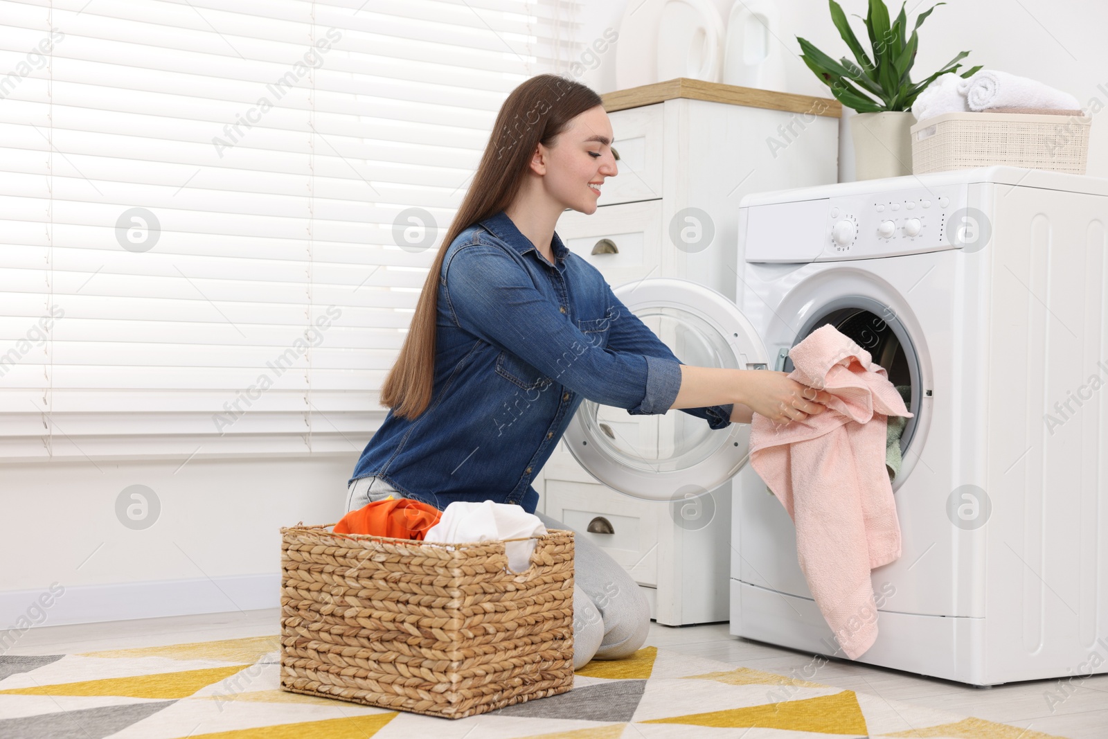 Photo of Woman putting dirty laundry into washing machine indoors