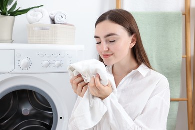 Photo of Woman with clean laundry near washing machine indoors