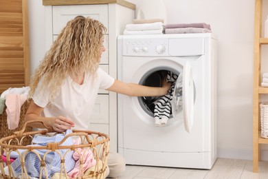 Photo of Woman putting dirty laundry into washing machine indoors