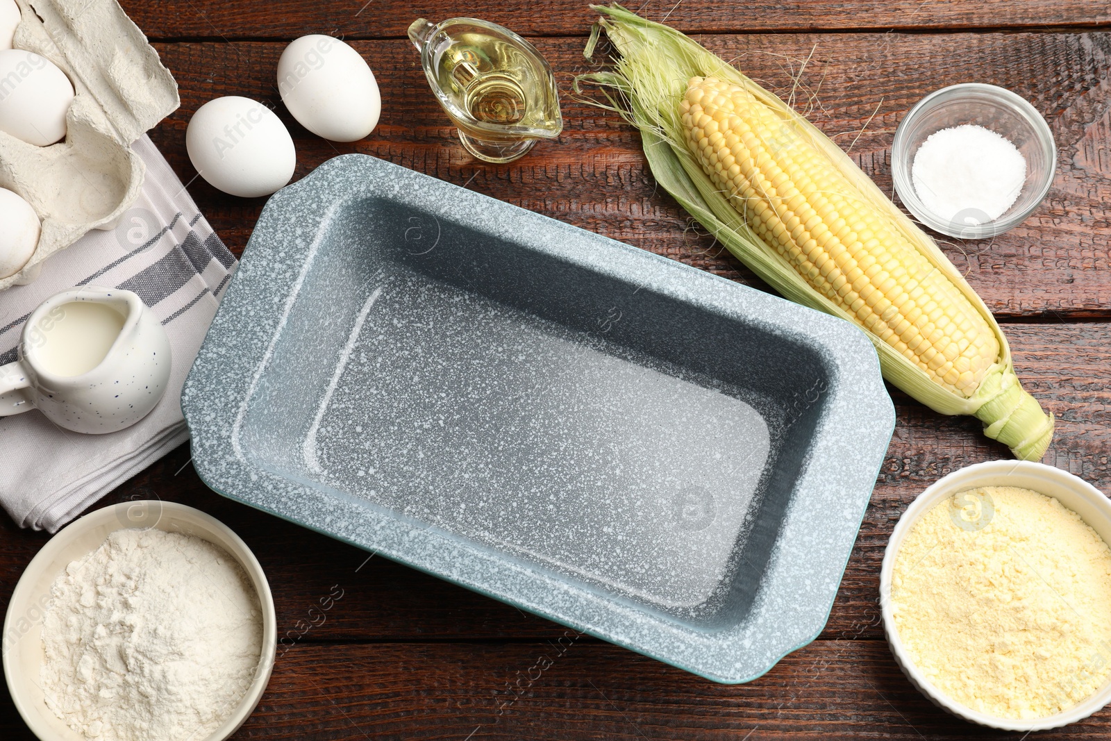 Photo of Baking dish surrounded by different ingredients for corn bread on wooden table, flat lay. Space for text