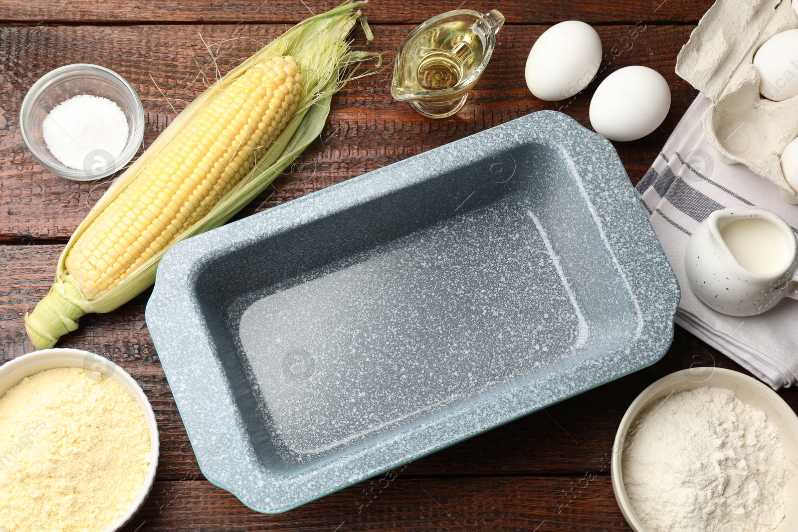 Photo of Baking dish surrounded by different ingredients for corn bread on wooden table, flat lay. Space for text