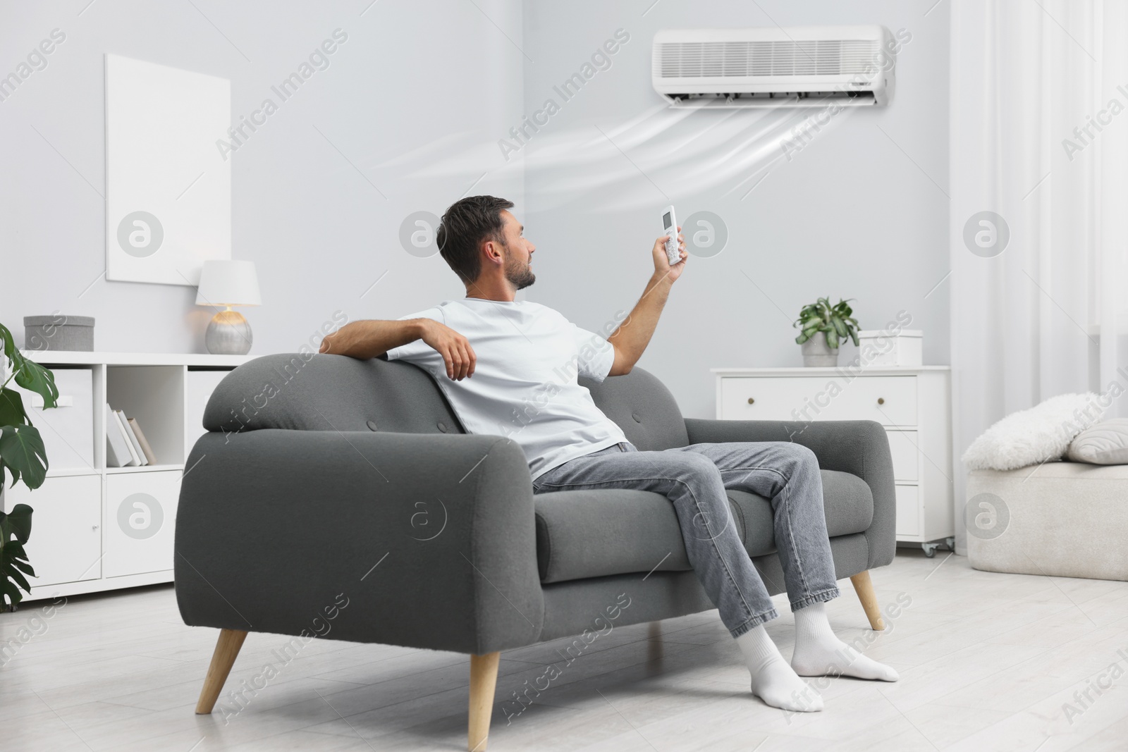 Image of Man using remote to control air conditioner on sofa at home