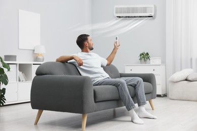 Image of Man using remote to control air conditioner on sofa at home