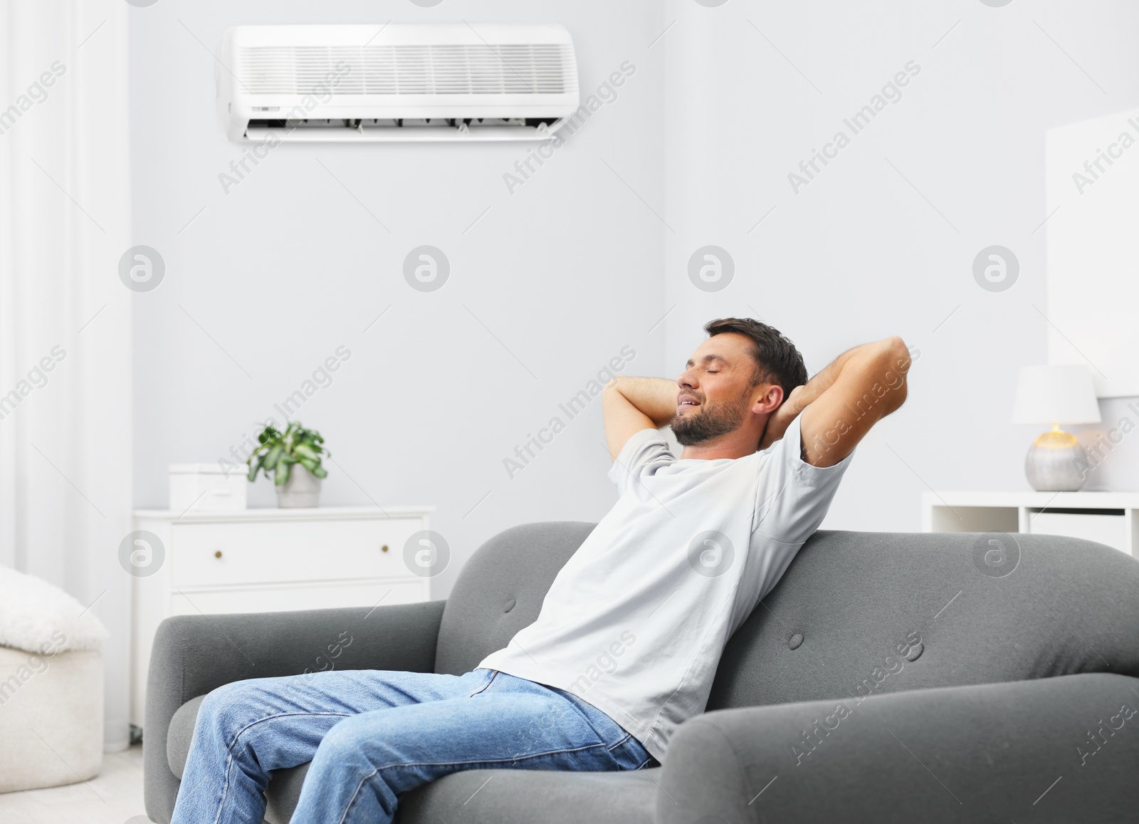 Happy man resting on sofa in room with air conditioner Image of Happy man resting on sofa in room with air conditioner