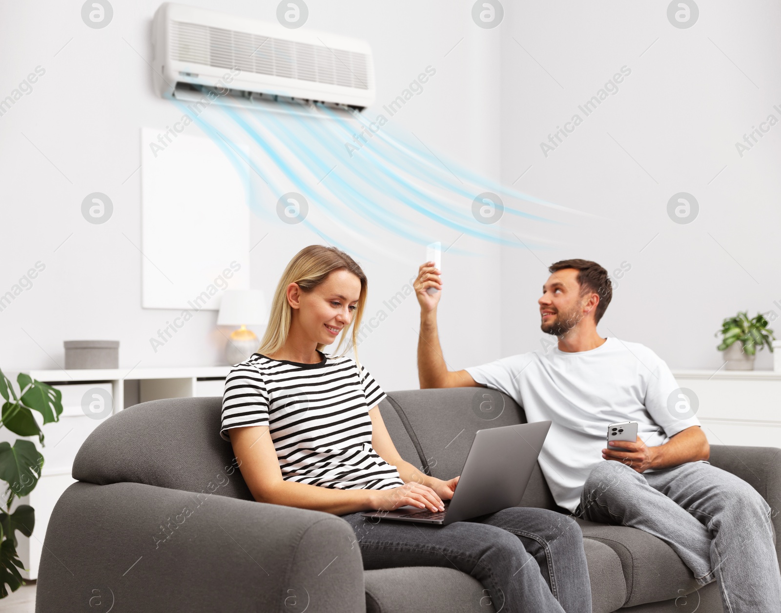 Image of Man using remote to control air conditioner and woman with laptop on sofa at home