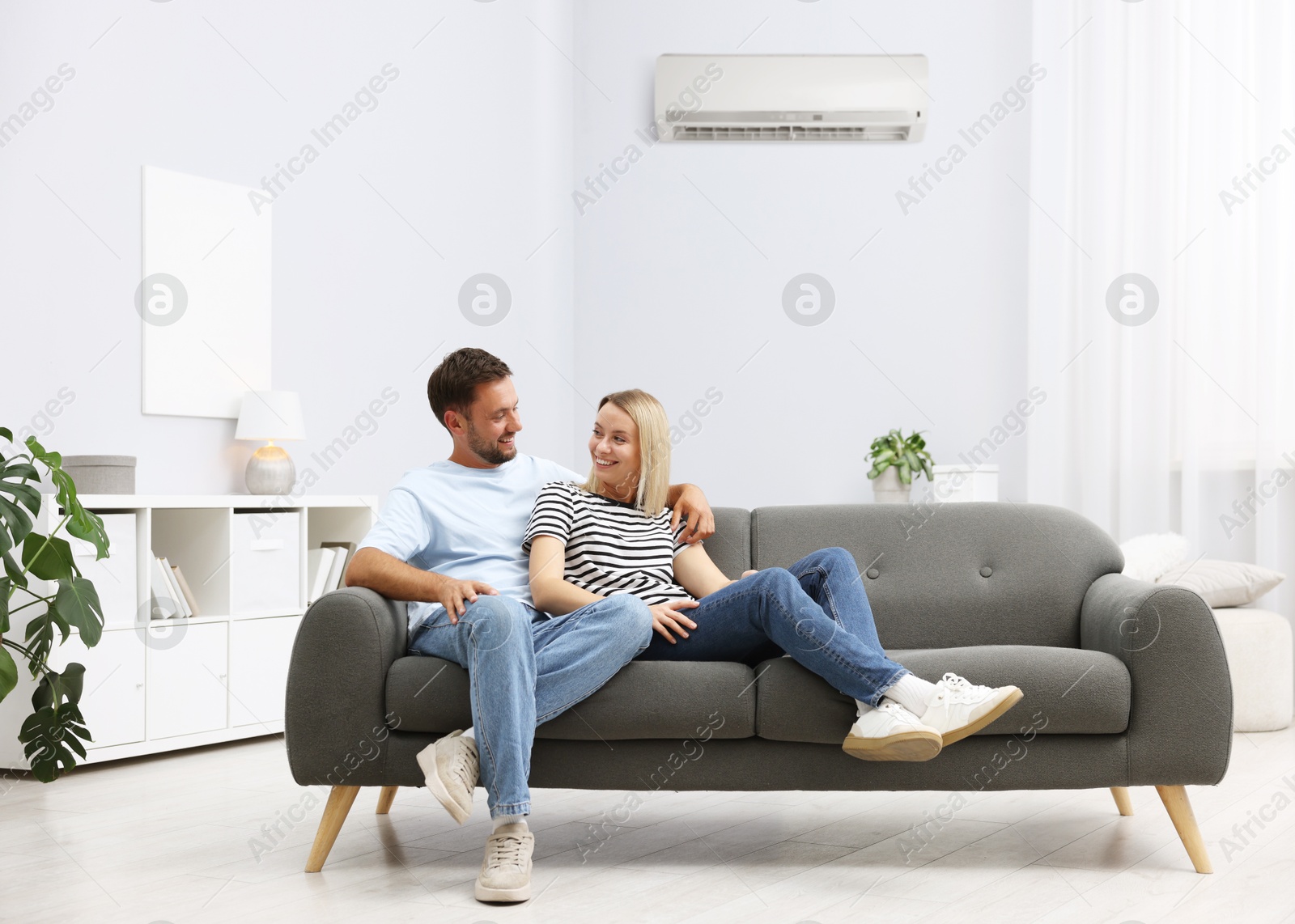 Image of Happy couple spending time together on sofa in room with air conditioner