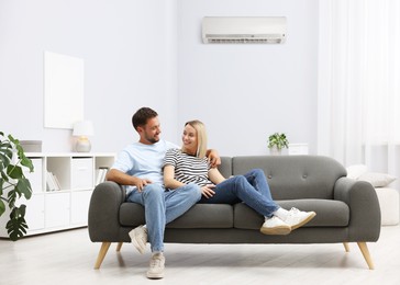 Image of Happy couple spending time together on sofa in room with air conditioner
