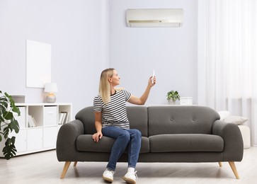 Image of Woman using remote to control air conditioner on sofa at home