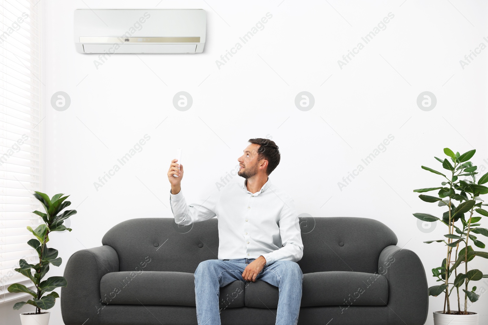 Image of Man using remote to control air conditioner on sofa at home