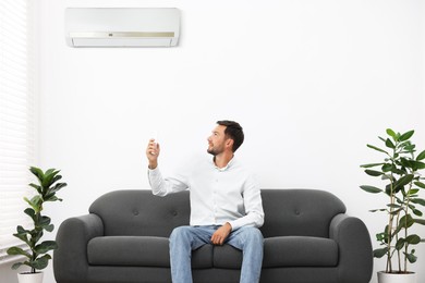 Image of Man using remote to control air conditioner on sofa at home