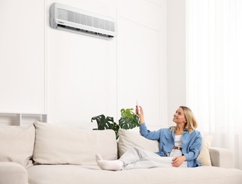 Image of Woman using remote to control air conditioner on sofa at home