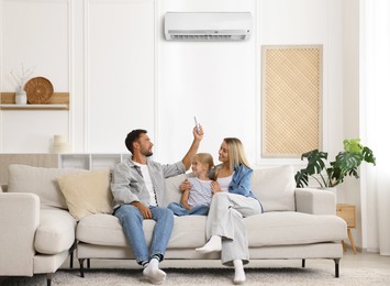 Image of Happy family on sofa at home. Man using remote to control air conditioner