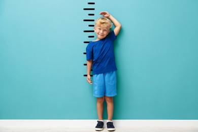 Image of Cute little boy measuring his height near turquoise wall with scale