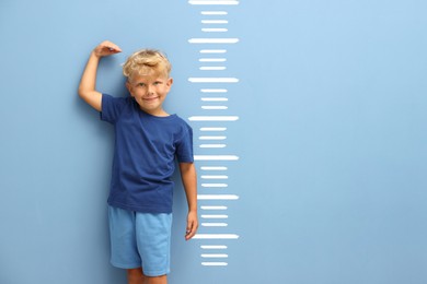 Image of Cute little boy measuring his height near light blue wall with scale