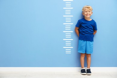 Image of Cute little boy measuring his height near blue wall with scale