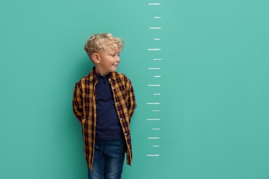 Image of Cute little boy measuring his height near turquoise wall with scale